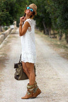 Woman wearing a white pom pom lace mini dress with sleeveless design and carrying a brown bag outdoors