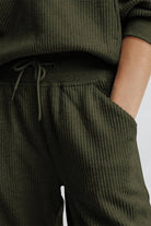 Close-up of unisex half-zip pullover and sweatpants set in olive green ribbed fabric with drawstring waist and hand in pocket