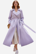 Timeless retro belted trench coat in lavender with double-breasted design and wide lapels, modeled with casual sneakers and a beige dress.