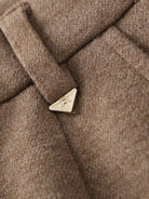 Close-up of brown thermal wool blend trousers fabric with gold triangular logo detail