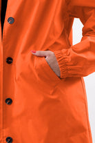 Close-up of orange water resistant oversized windbreaker with button closure and elastic cuff pocket detail