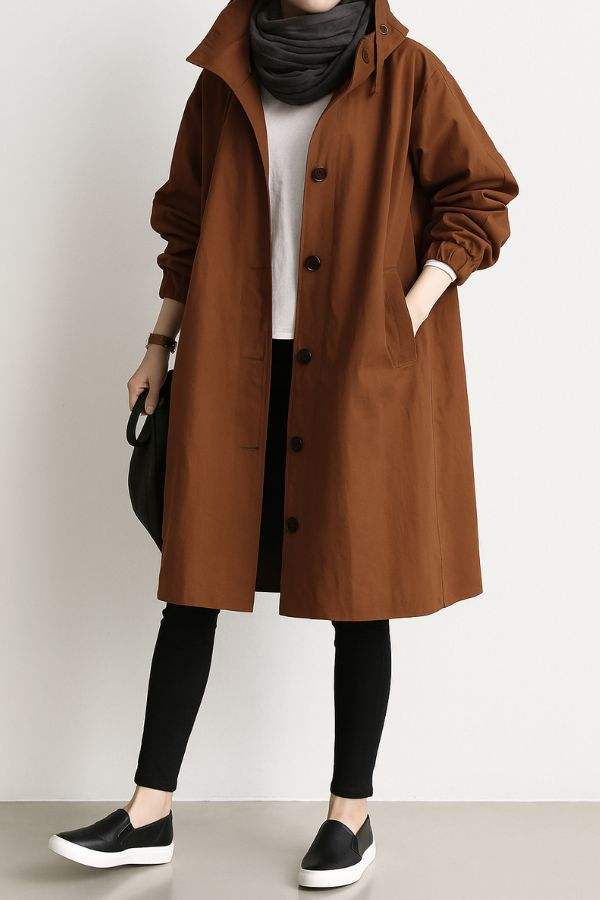 Woman wearing brown water-resistant oversized hooded windbreaker rain jacket with black scarf and black leggings