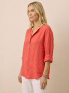 woman wearing coral pure linen age-defying button detail shirt with rolled sleeves and white pants