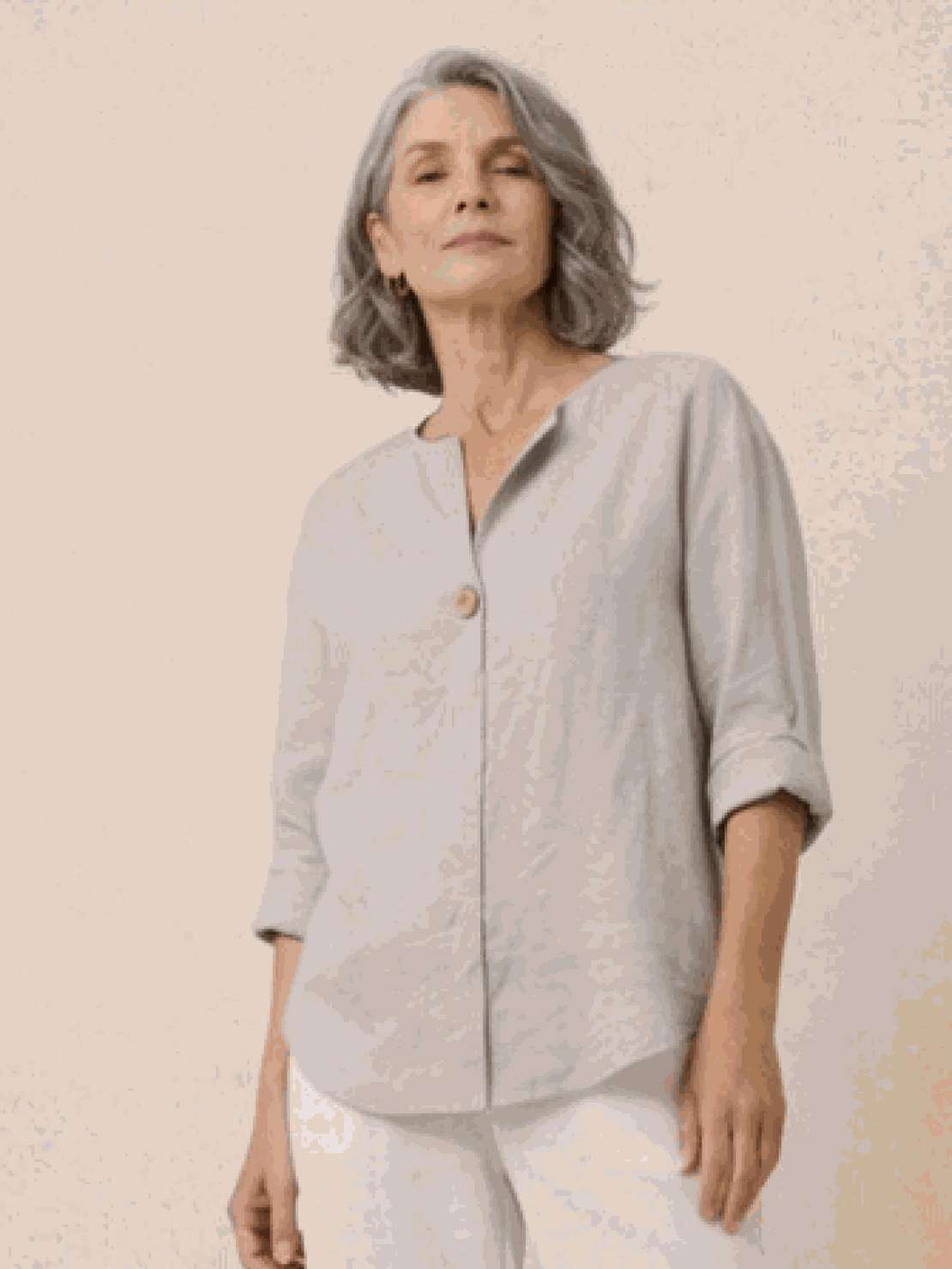 Woman wearing a pure linen age-defying button detail shirt in soft beige, showcasing breathable and elegant fabric design