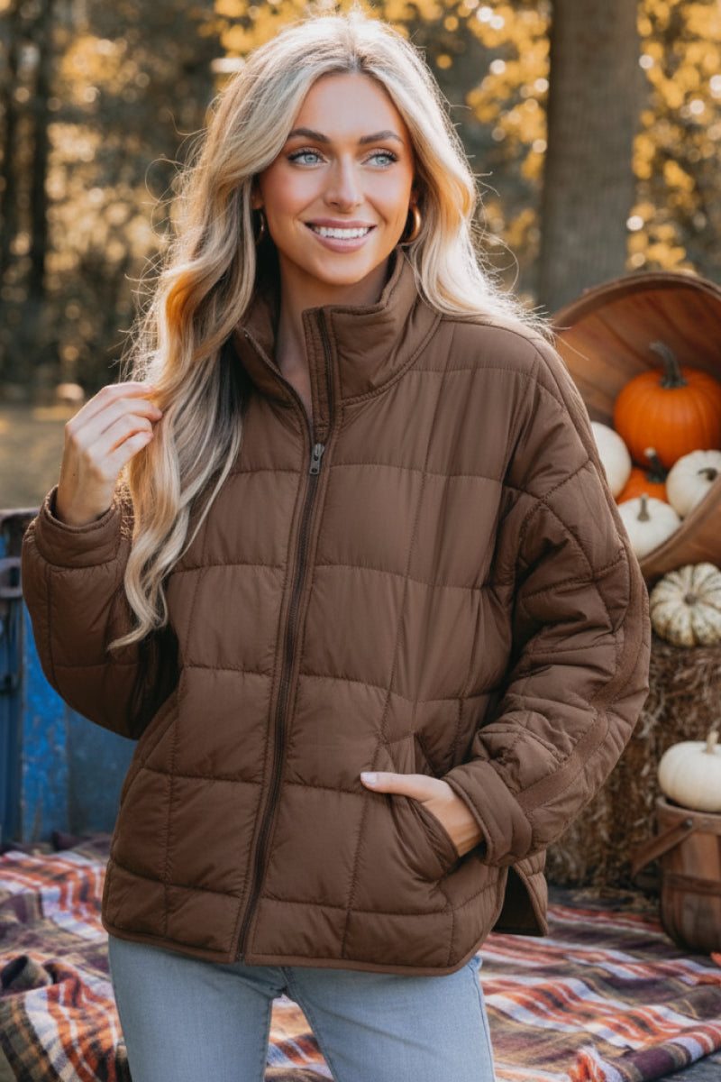 Woman wearing lightweight brown puffer travel jacket outdoors with autumn decorations