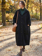 Woman wearing oversized black water-resistant windbreaker jacket with hood, large pockets, and snap-button closure in autumn park setting