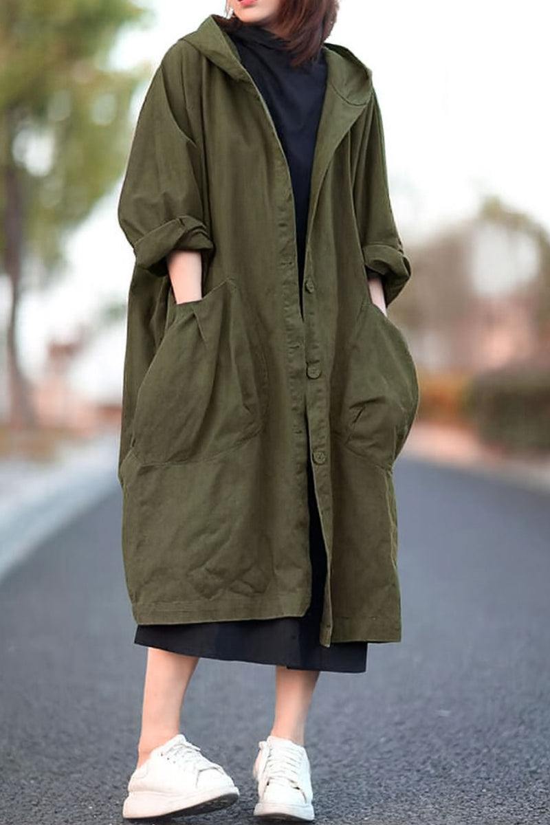 Oversized olive green Heritage Windbreaker Jacket with attached hood and large front pockets, worn over black dress and white sneakers.