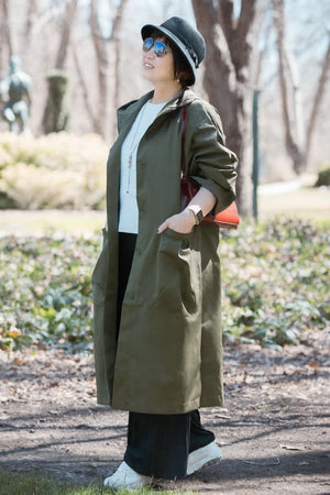 Woman wearing oversized olive green waterproof windbreaker jacket with hood in outdoor setting