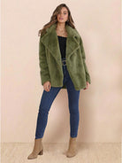 Woman wearing an open front oversized green faux fur jacket with draped collar and mid-hip length paired with jeans and ankle boots