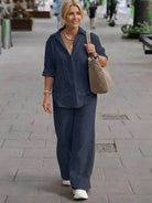 Woman wearing oversized 100% cotton navy blue shirt and wide-leg pants co-ord set walking on city street with beige tote bag and white sneakers