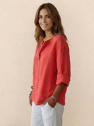 Woman wearing coral pure linen age-defying shirt with button detail and white pants