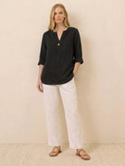Woman wearing black pure linen age-defying shirt with button detail and white pants.