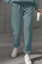 Woman wearing light green cotton blend tracksuit pants with white sneakers walking outdoors holding a coffee cup