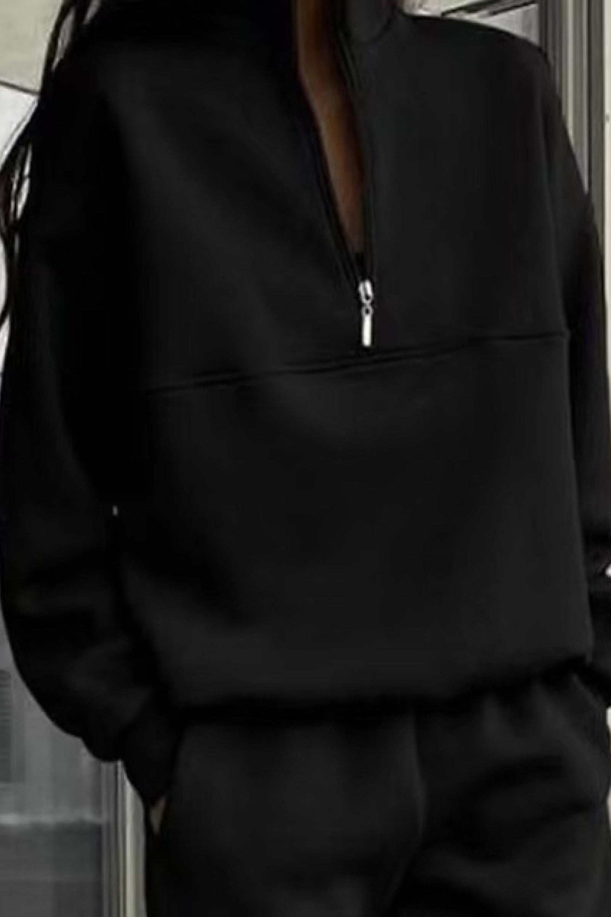Woman wearing a black cotton blend tracksuit with a half-zip high collar and relaxed fit