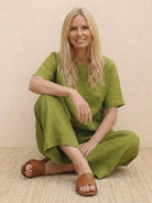 Woman wearing green loose fit co-ord set with short sleeves and wide-leg pants sitting cross-legged on floor in brown sandals