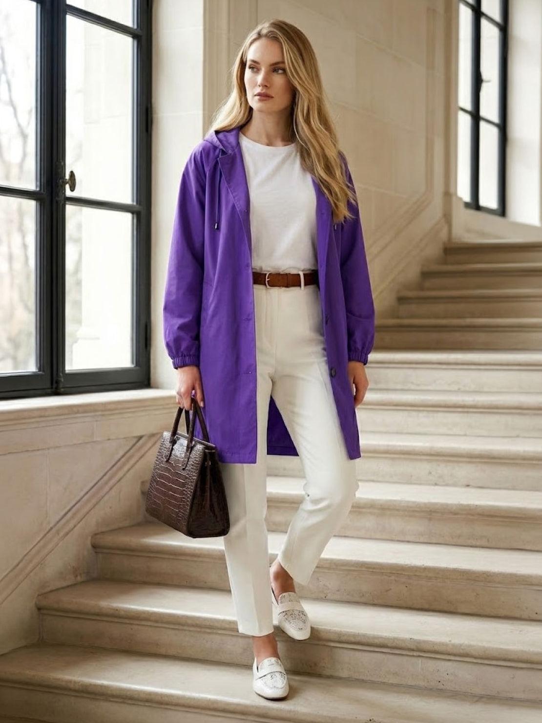 Woman wearing purple Rain Couture Windbreaker with white pants and carrying brown handbag indoors