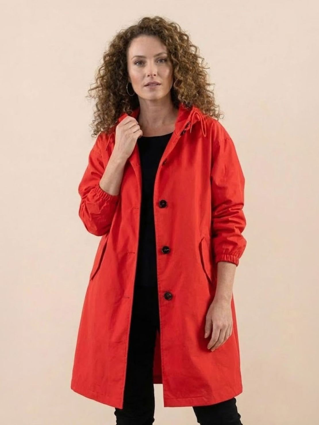 Woman wearing red oversized Rain Couture Windbreaker jacket with black outfit underneath against neutral background